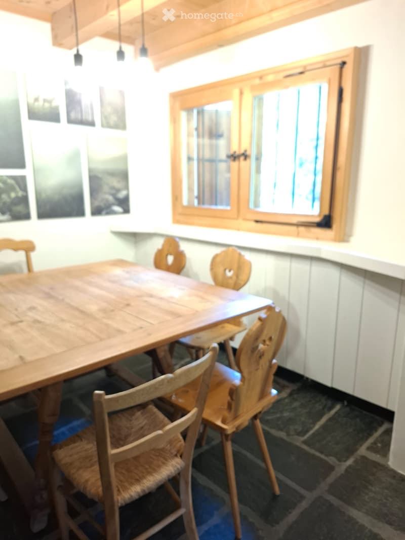 A cozy dining area with a wooden table and chairs, featuring a large window with wooden frames and several framed pictures on the wall.