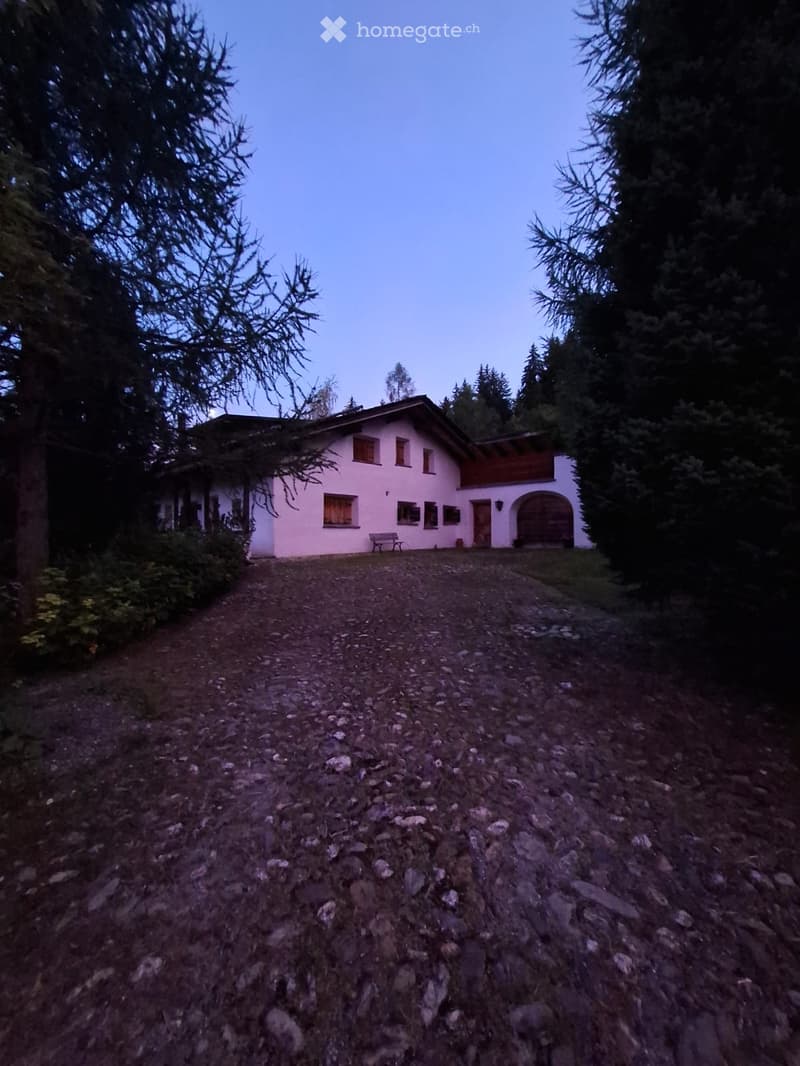A two-story white house with a red roof, surrounded by trees and a gravel driveway.