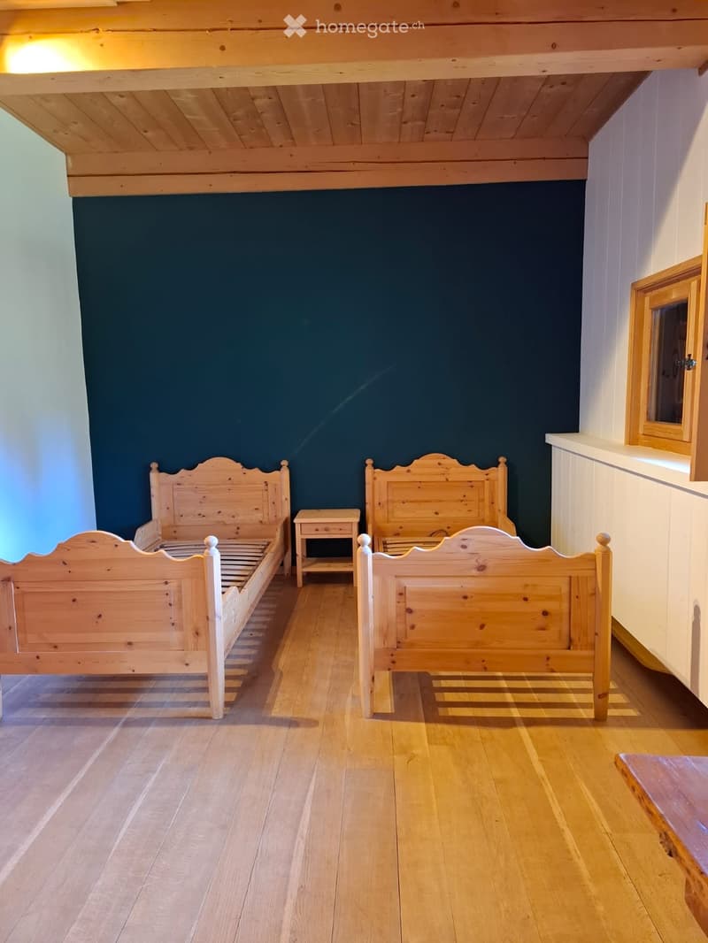 Bright bedroom with wooden floors, two wooden beds with headboards, and a small nightstand between them.