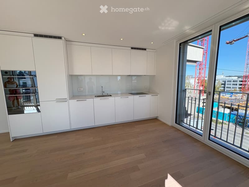 Modern kitchen with white cabinets, wooden flooring, and large windows overlooking a construction site.