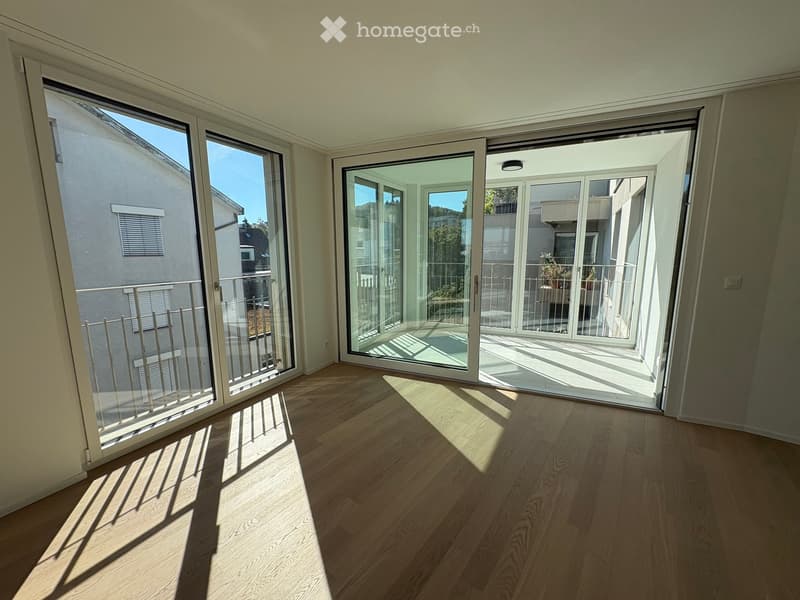 Empty room with wooden flooring and large sliding glass doors leading to a balcony. The room is well-lit with natural light and has a modern design.