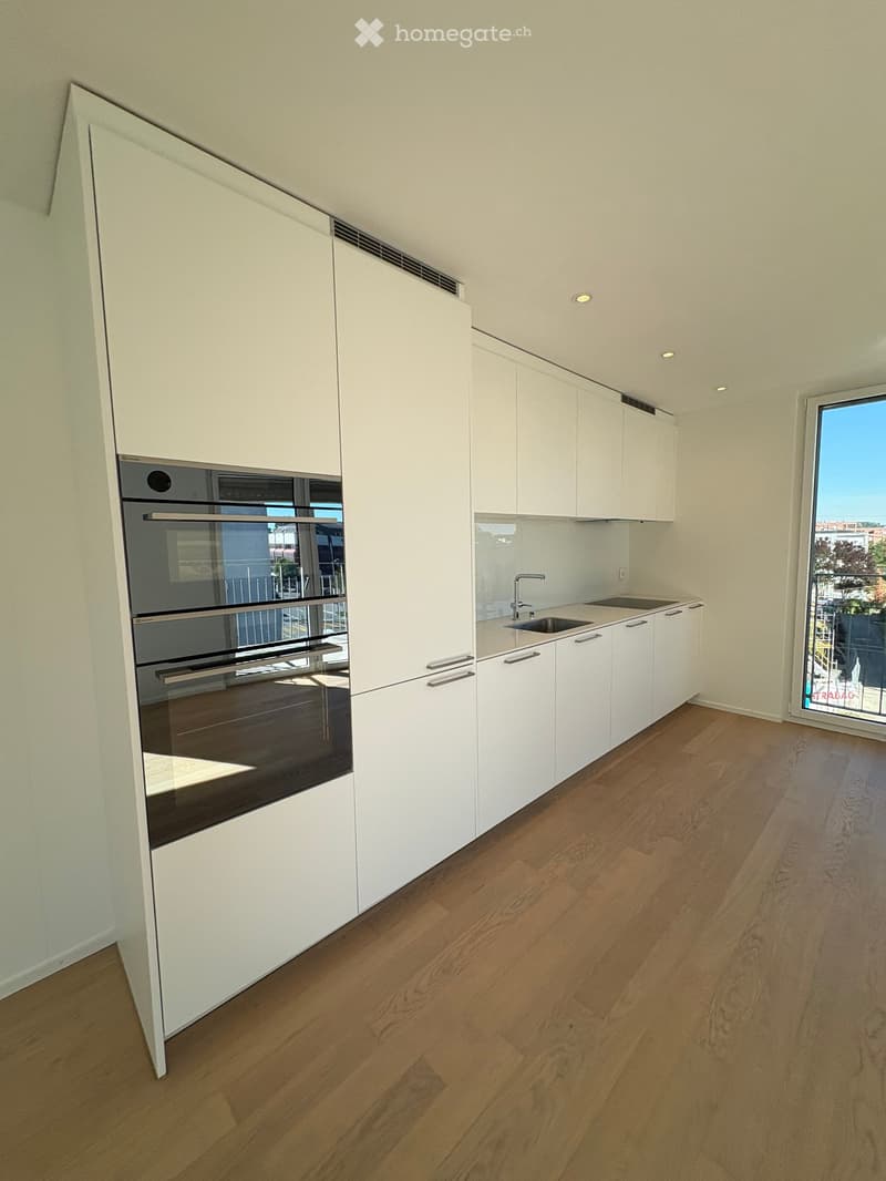 Modern kitchen with white cabinets, wooden flooring, built-in oven, and a sink with a faucet.