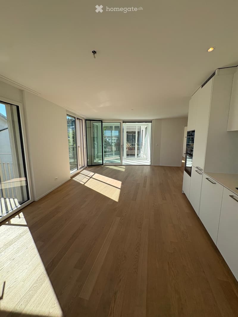 Empty room with light wooden flooring, white walls, and large glass sliding doors leading to a balcony.