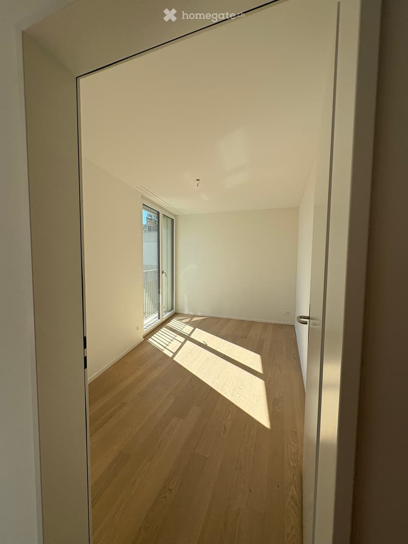 Empty hallway with wooden flooring, white walls, and a glass door leading to a balcony.