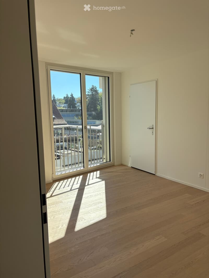 Empty room with wooden flooring, white walls, and large sliding glass doors leading to a balcony or outdoor area.