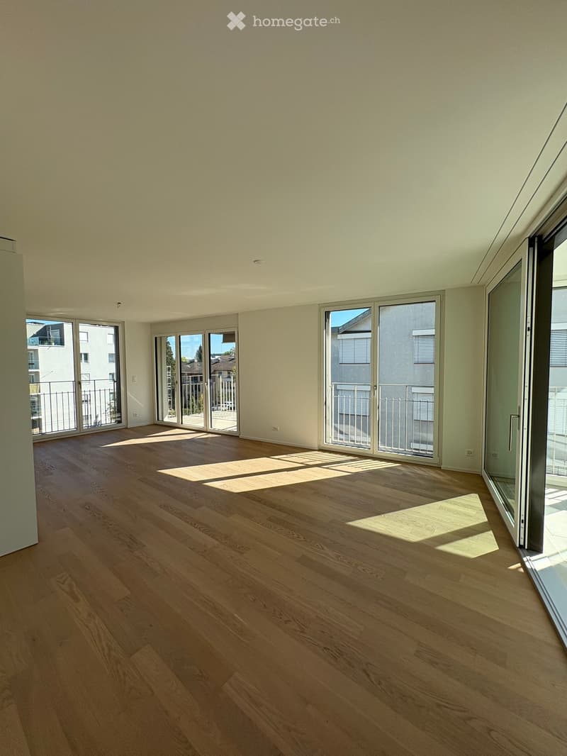 Empty room with wooden flooring, large windows, and sliding glass doors leading to a balcony.