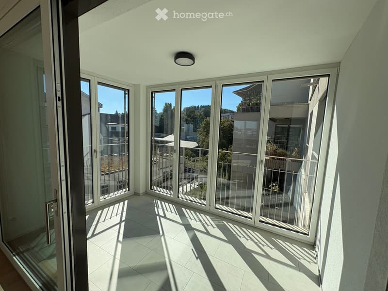 Bright, modern balcony with large glass doors, tiled floor, and a view of the surrounding area.