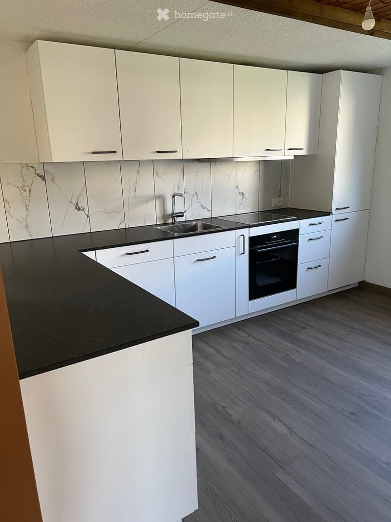 Modern kitchen with white cabinets, black countertops, a sink, and an oven. The backsplash features a marble design.