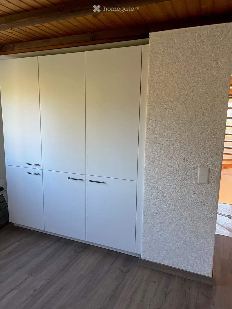 Modern kitchen with white cabinets and wooden flooring, featuring a textured wall and visible light switch.