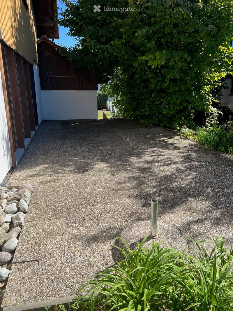 Gravel pathway leading to a building entrance, surrounded by greenery and rocks.
