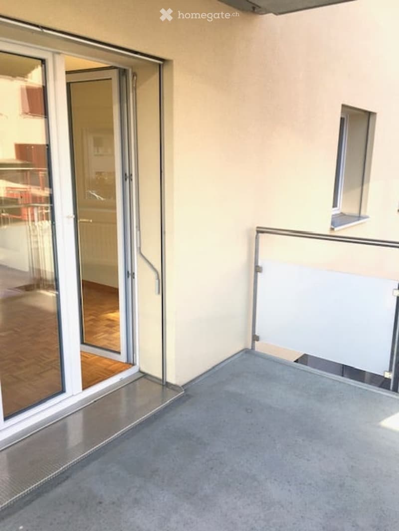 Empty balcony with glass sliding doors leading to an interior space, metal railing, and a small window on the adjacent wall.