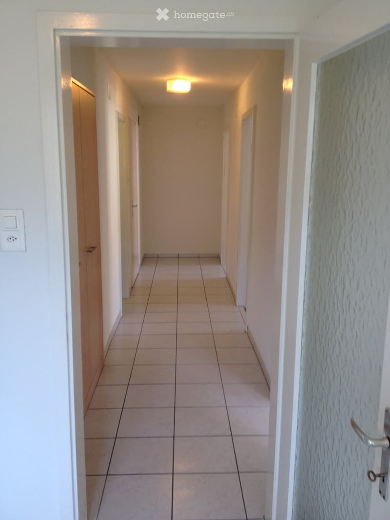 Empty hallway with tiled floor, white walls, and recessed lighting. Doors visible on both sides.