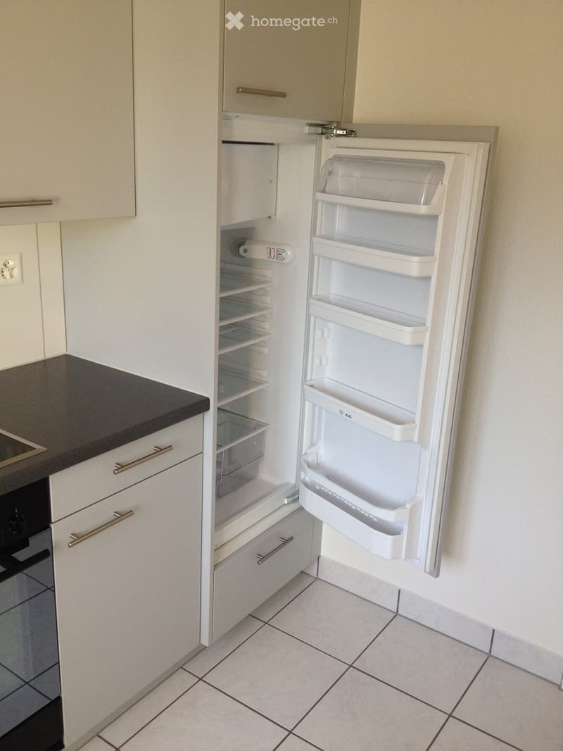 Modern kitchen with white cabinets, a black countertop, and an open refrigerator showing empty shelves and drawers.