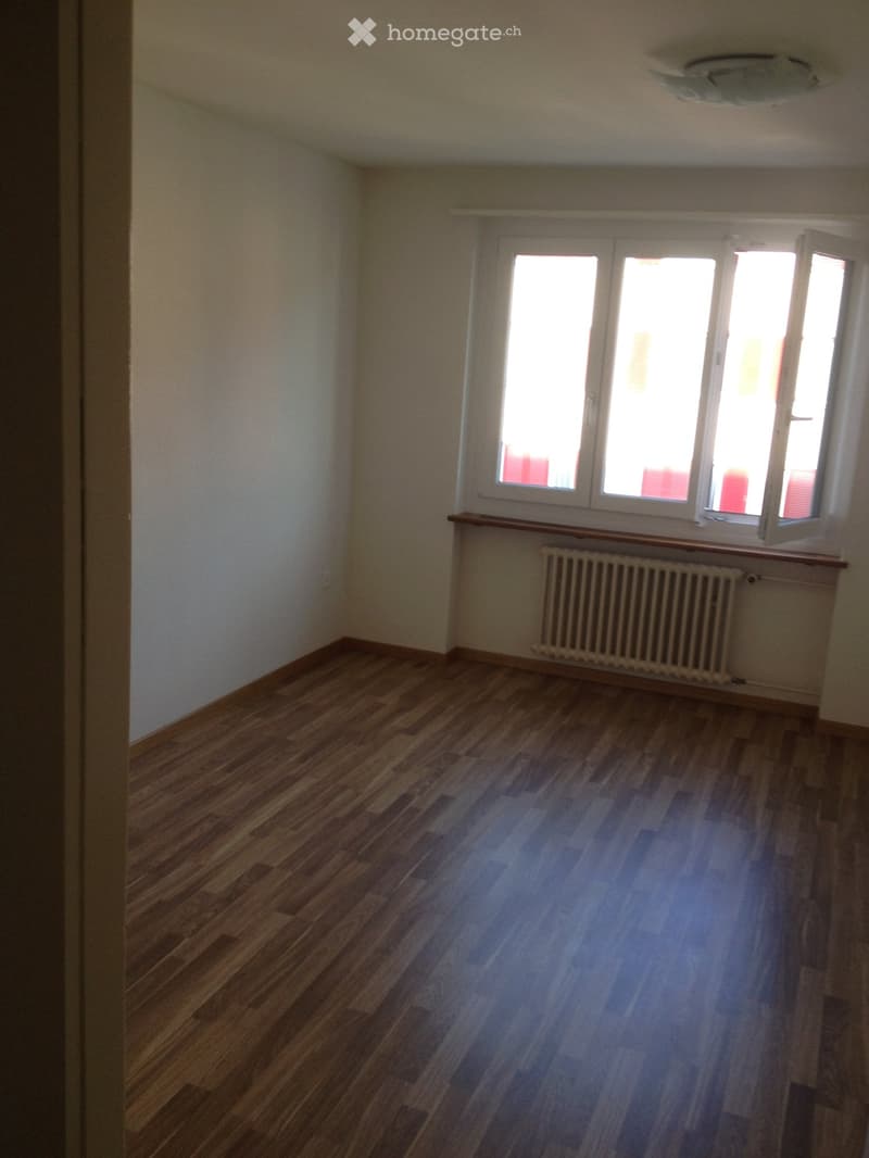 Empty room with wooden flooring, white walls, and a window with a radiator below it.