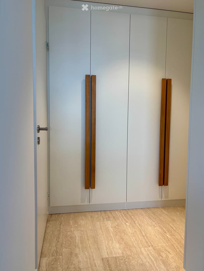 Empty room with light-colored wooden flooring and white cabinetry with wooden handles.