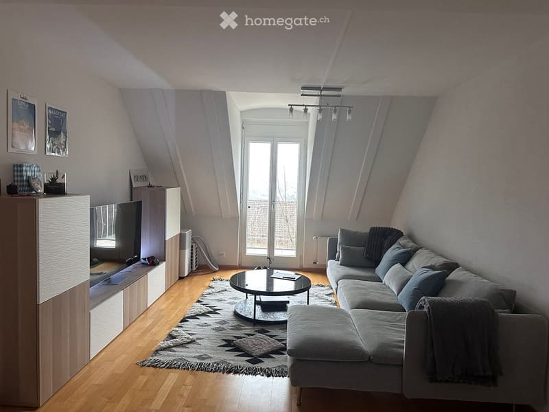 L-shaped sofa, round coffee table, large rug, mounted TV on wall, sliding glass doors, sloped ceiling, decorative items on shelves