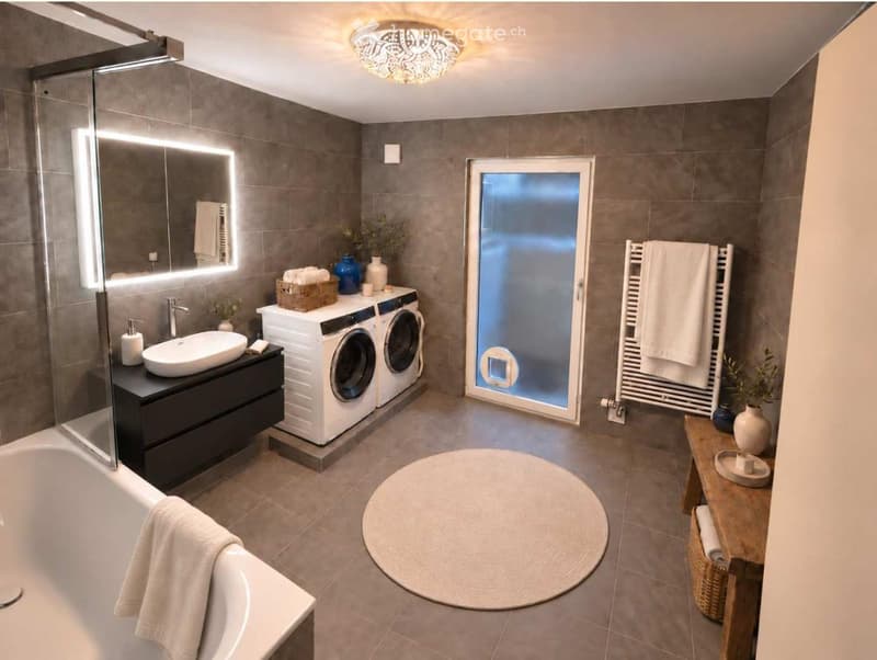 Modern bathroom with a bathtub, sink, mirror, washing machine, dryer, towel rack, round rug, wooden shelf, and decorative vases.