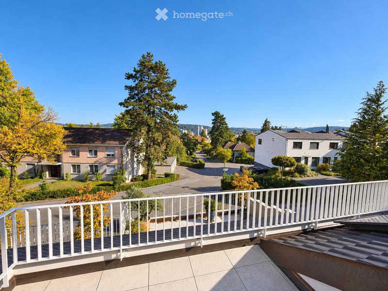 Balcony with white railing overlooking a residential neighborhood with houses, trees, and a clear blue sky.