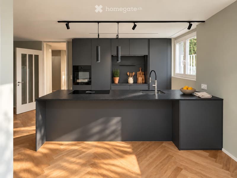 Modern kitchen with dark grey cabinetry, a central island, pendant lights, and a sleek black countertop.
