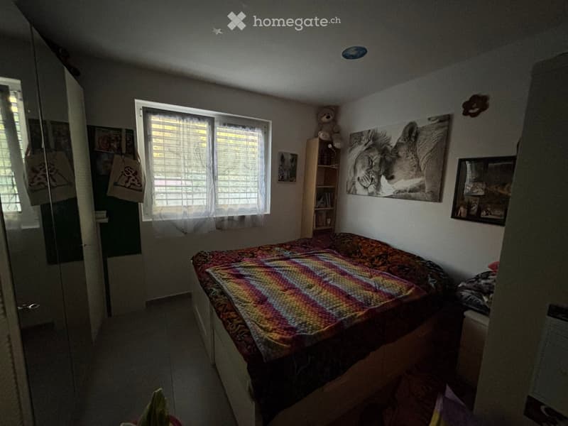 Bedroom with a single bed, colorful bedspread, nightstand, bookshelf, and wall decorations including a large animal print picture and framed photos.
