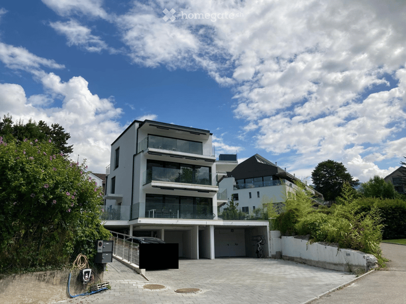 Modern two-story house with white exterior, large glass balconies, and a covered garage. The house features contemporary design with clean lines and large windows.