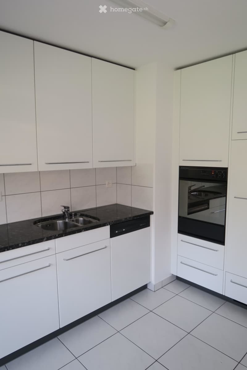 Modern kitchen with white cabinets, black granite countertops, stainless steel sink, dishwasher, and oven.