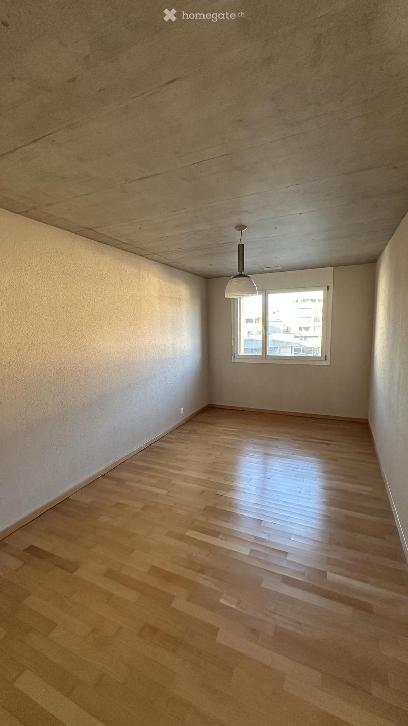Empty room with wooden flooring, white walls, and a single window with white frame. A modern pendant light hangs from the ceiling.