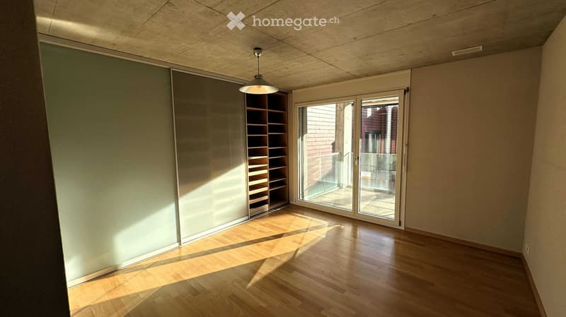 Empty room with wooden flooring, built-in shelving unit, and large sliding glass doors leading to a balcony.
