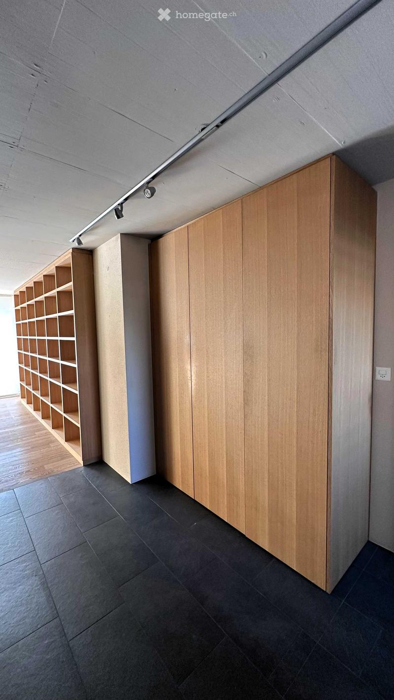Empty room with dark tiled floor, light wooden built-in cabinets, and a wooden shelving unit. The walls are painted in neutral tones, and the ceiling has recessed lighting.