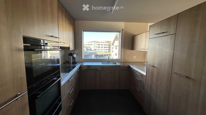 Modern kitchen with light wood cabinets, stainless steel appliances, and a large window overlooking a cityscape.