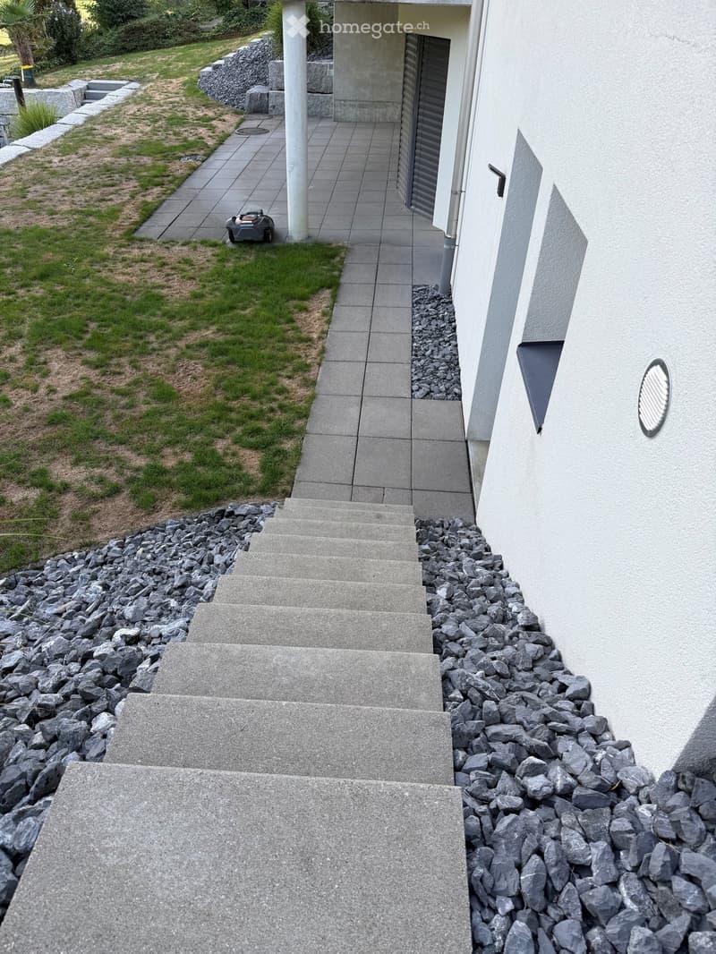 Concrete steps leading up to a modern house entrance, surrounded by gravel and grass.
