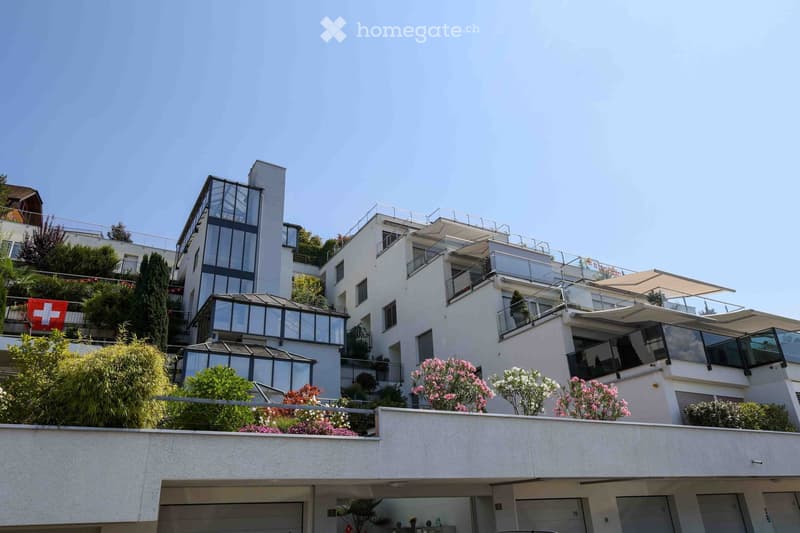 Modern multi-story residential building with balconies, glass sections, and surrounding greenery.