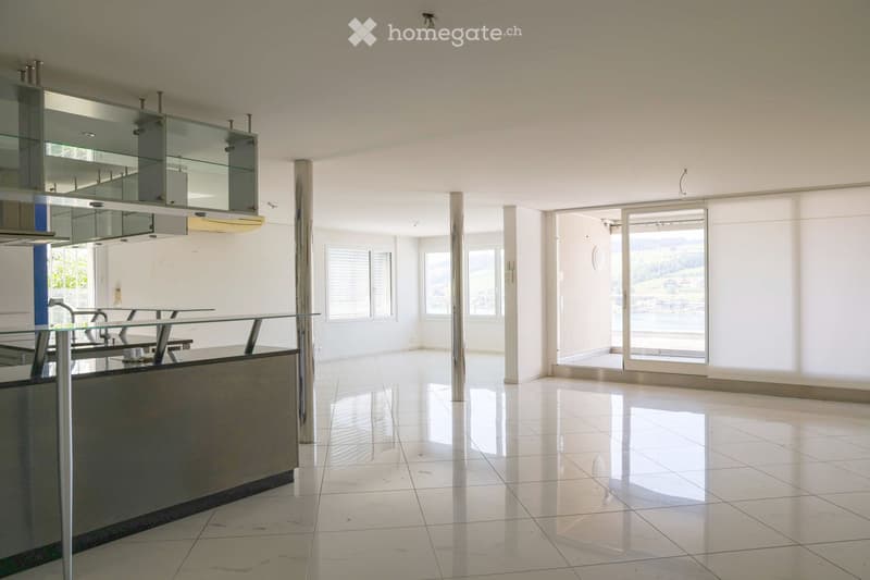 Modern kitchen with white tiled floors, glass cabinets, a kitchen island, and a large window offering a scenic view.