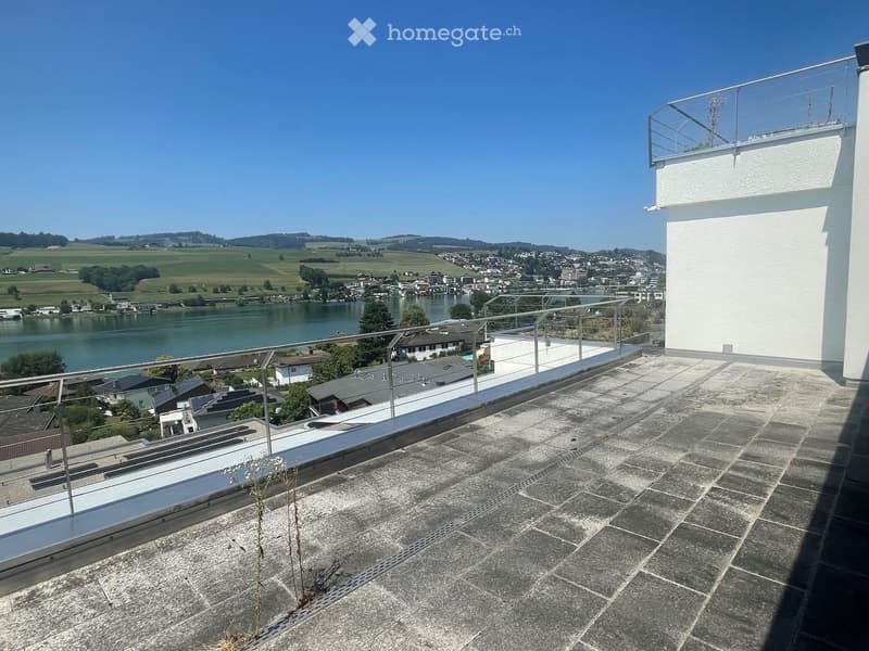 Roof terrace with stone tiles, metal railing, and scenic view of a lake and town.