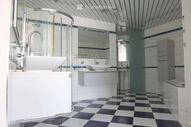 Modern bathroom with white tiles, checkered floor, double sinks, large mirror, and a glass-enclosed shower area.