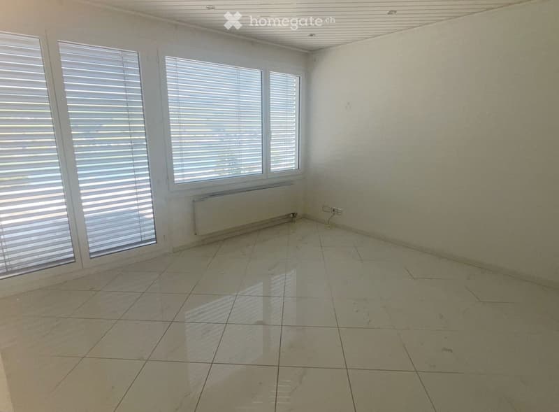 Empty room with tiled floor, white walls, large windows with blinds, and a radiator under the windows.