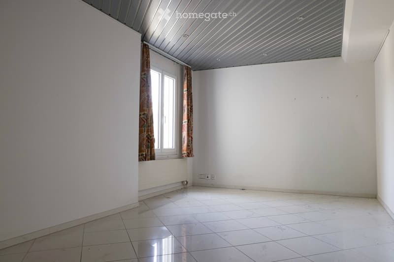 Empty room with white tiled floor, white walls, and a window with patterned curtains. The ceiling has a modern, ribbed design.