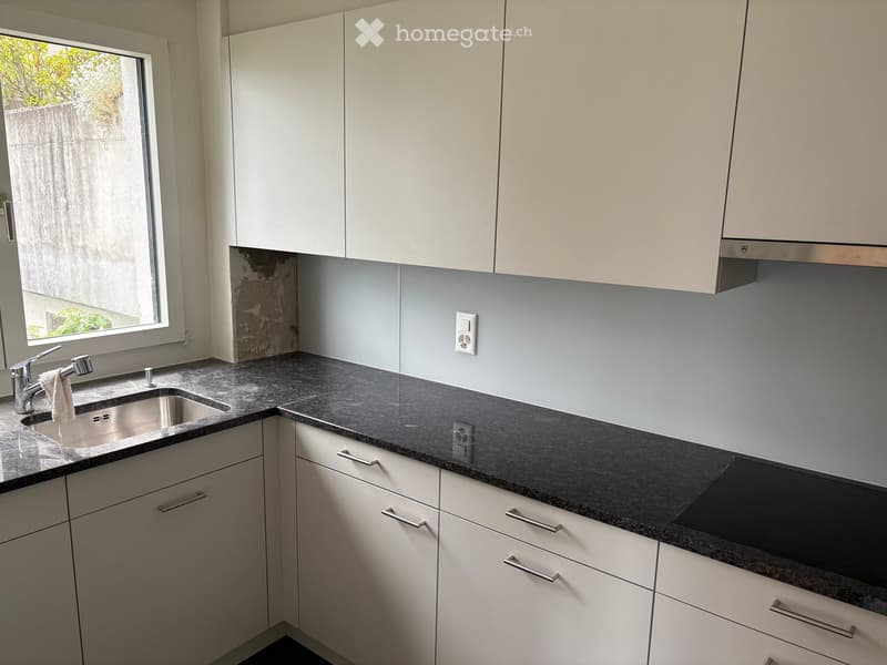 Modern kitchen with white cabinets, dark granite countertop, stainless steel sink, and a window with a view of greenery.