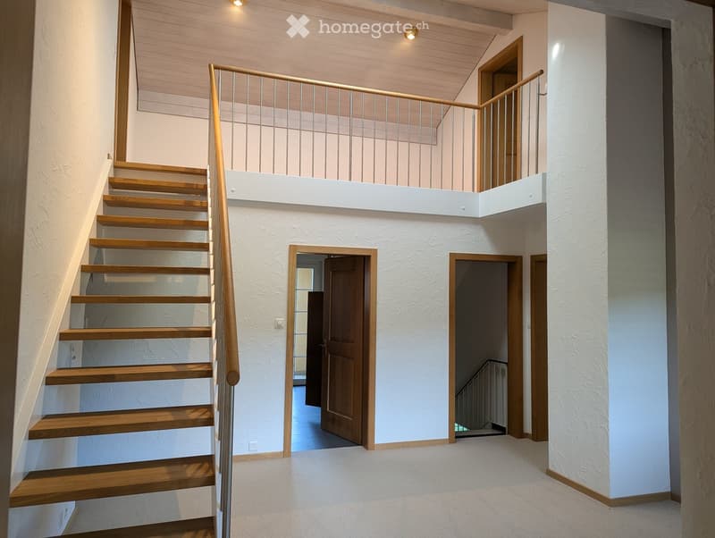 Modern staircase with wooden steps and metal railing, leading to an upper level with white walls and wooden doors.