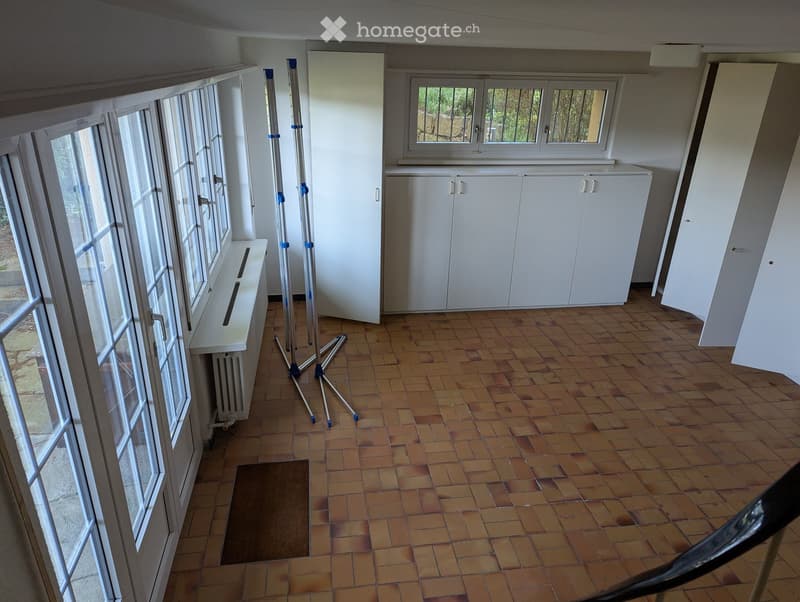 Empty room with tiled floor, white walls, large windows, radiator, and white cabinetry.