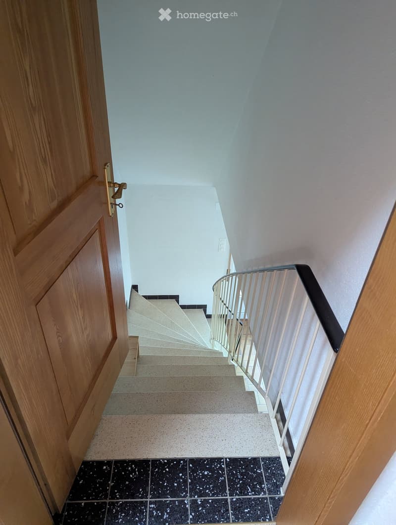 Spiral staircase with white walls and a wooden door on the left side.