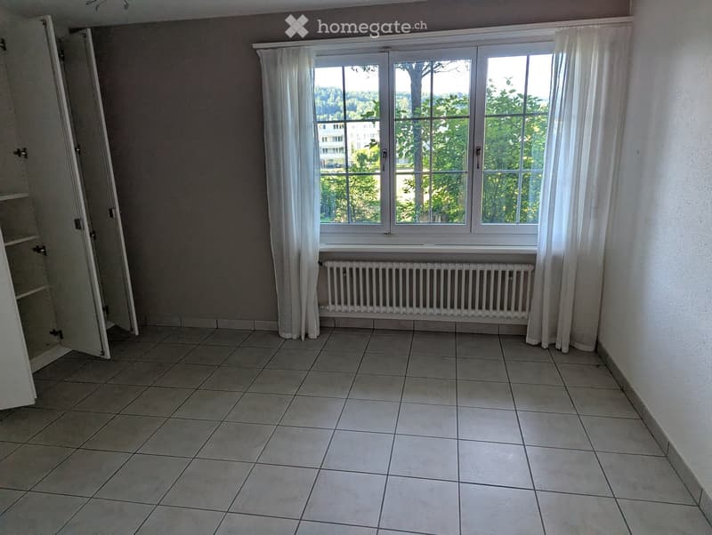Empty room with tiled floor, large window with white curtains, radiator, and open closet door.