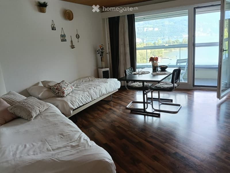 Cozy bedroom with a sofa bed, small table, chairs, and a scenic view through large windows.