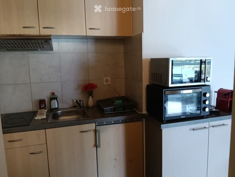 Modern kitchen with light wooden cabinets, stainless steel appliances, and a sink with a faucet. Includes a microwave, oven, and various small items on the counter.