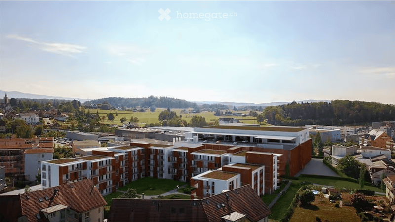 Aerial view of a modern residential complex with multiple buildings, surrounded by green spaces and a rural landscape.