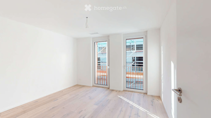Empty room with white walls, light wooden flooring, and two glass doors leading to a balcony area.