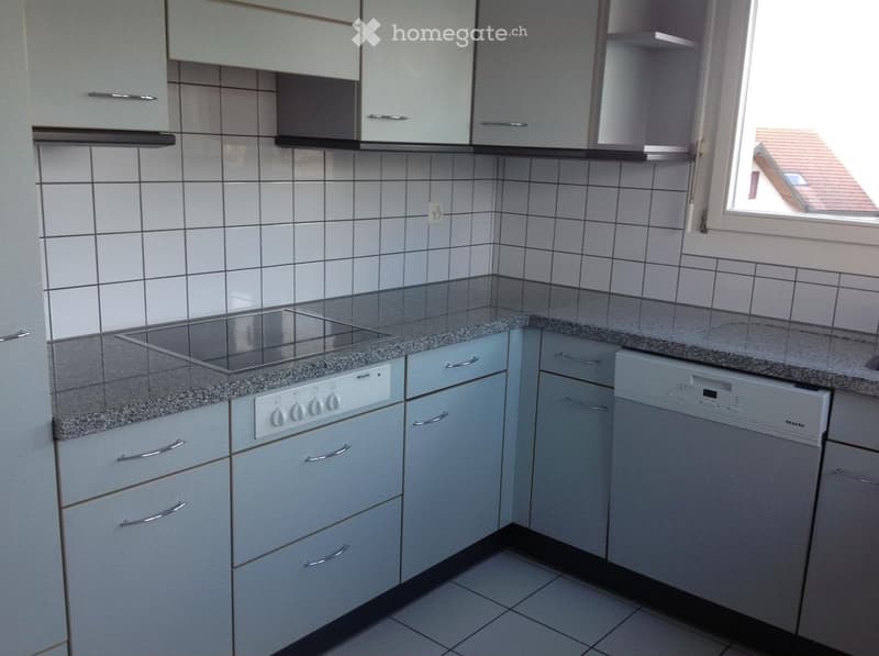 Modern kitchen with white cabinets, granite countertops, a built-in stove, and a dishwasher. The walls are tiled, and there is a window providing natural light.