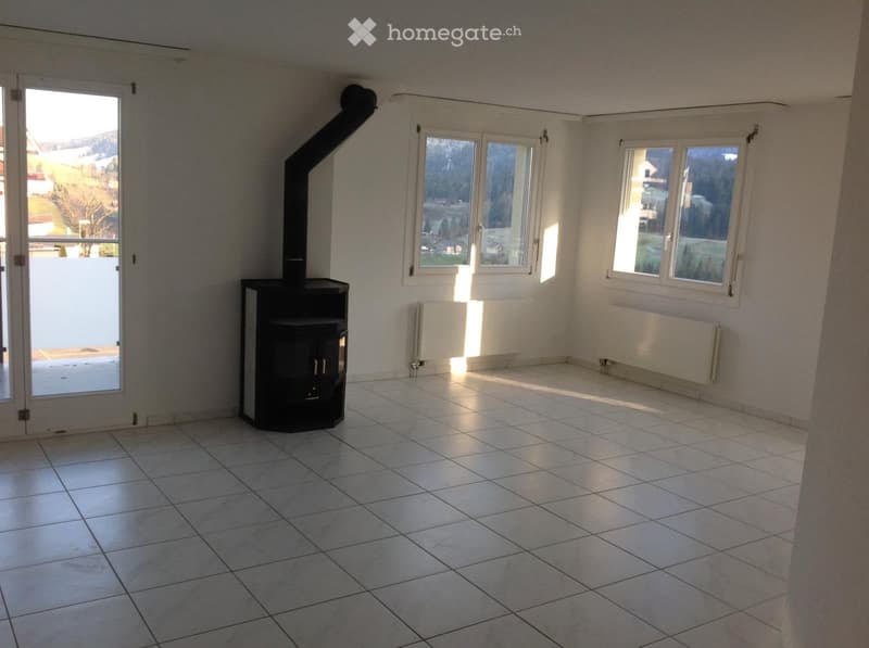 Empty room with tiled floor, white walls, large windows, and a black wood-burning stove with a chimney.