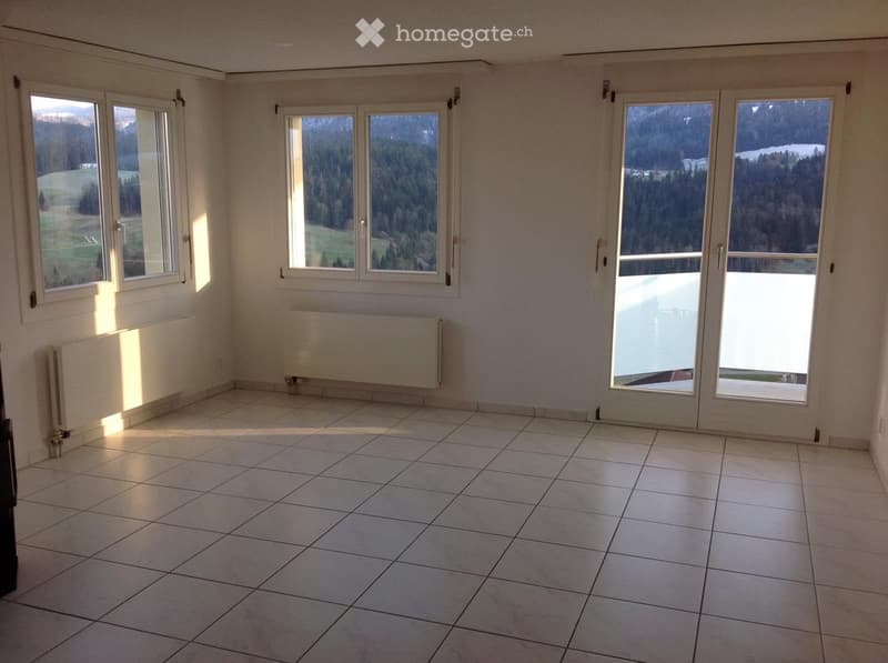 Empty room with tiled floor, large windows, radiators, and a sliding glass door leading to a balcony.