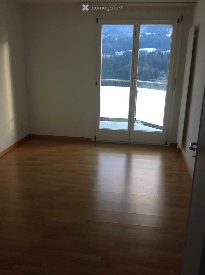 Empty room with wooden flooring and large sliding glass doors leading to a balcony with a scenic mountain view.